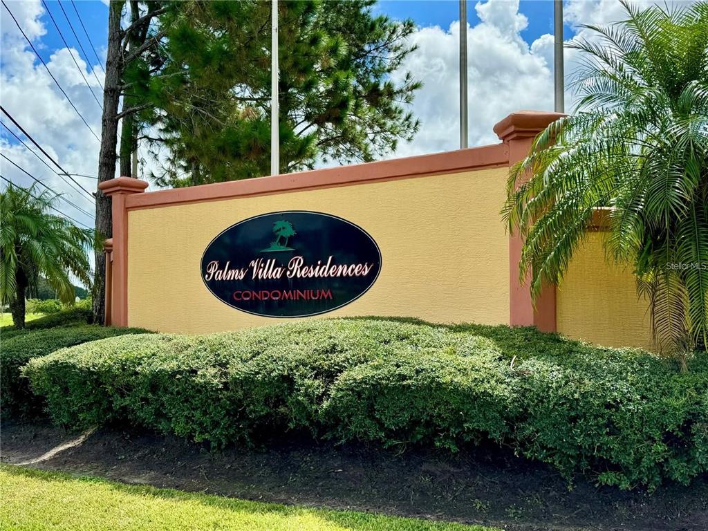 A yellow stucco monument sign for Palms Villa Residences stands behind a manicured hedge — 10831 WINDSOR WALK DRIVE UNIT 1210, ORLANDO, FL