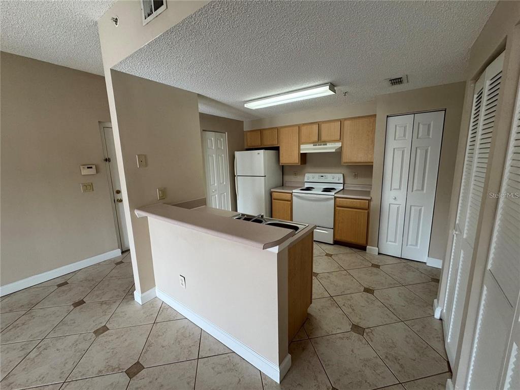 A kitchen with light wood cabinets, white appliances, and a breakfast bar on tiled floors — 10831 WINDSOR WALK DRIVE UNIT 1210, ORLANDO, FL