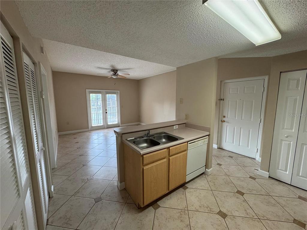 A kitchen island with a double sink and dishwasher overlooks a living area with tile floors — 10831 WINDSOR WALK DRIVE UNIT 1210, ORLANDO, FL
