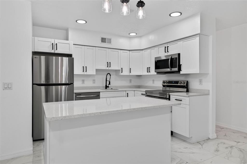 A modern kitchen features white cabinets, stainless steel appliances, and a central quartz-topped island — 2801 45TH STREET S, ST PETERSBURG, FL