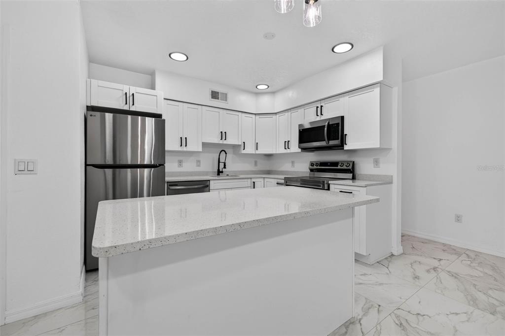 A modern kitchen features white cabinets, stainless steel appliances, a quartz island, and marble-look flooring — 2801 45TH STREET S, ST PETERSBURG, FL