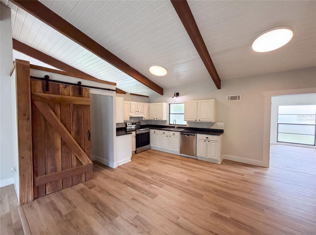A kitchen features white cabinets, dark countertops, wood-look flooring, and a rustic sliding barn door — 925 PARK PLACE, DELAND, FL