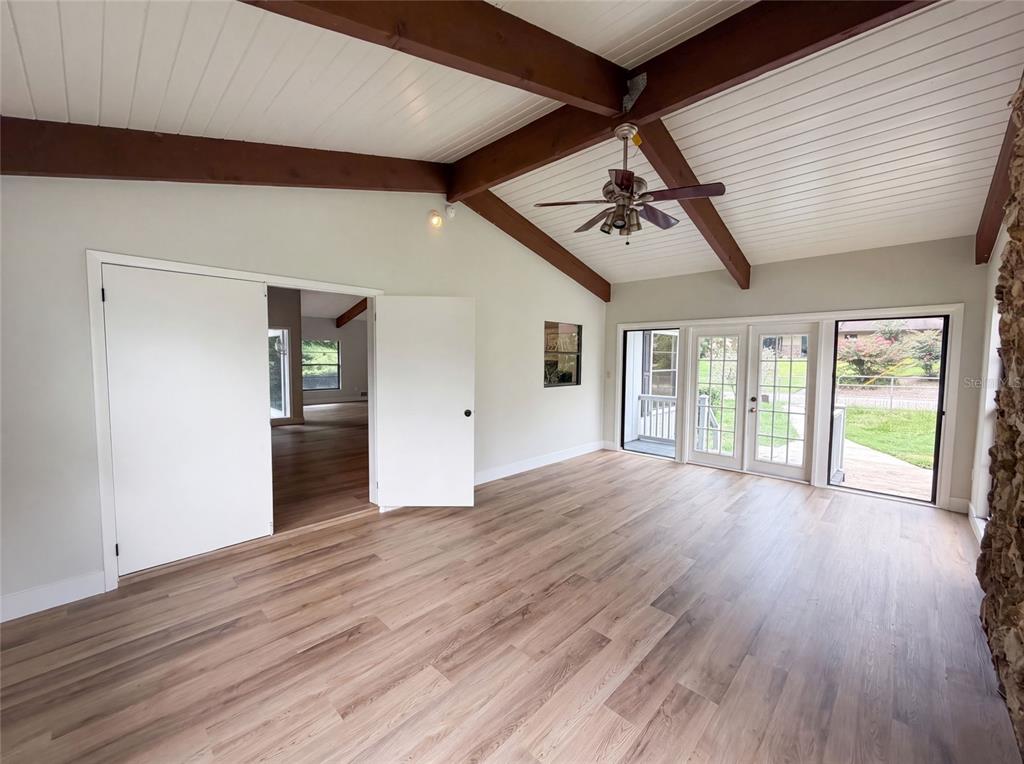 A living room features vaulted ceilings with exposed beams, wood-look flooring, and glass patio doors — 925 PARK PLACE, DELAND, FL