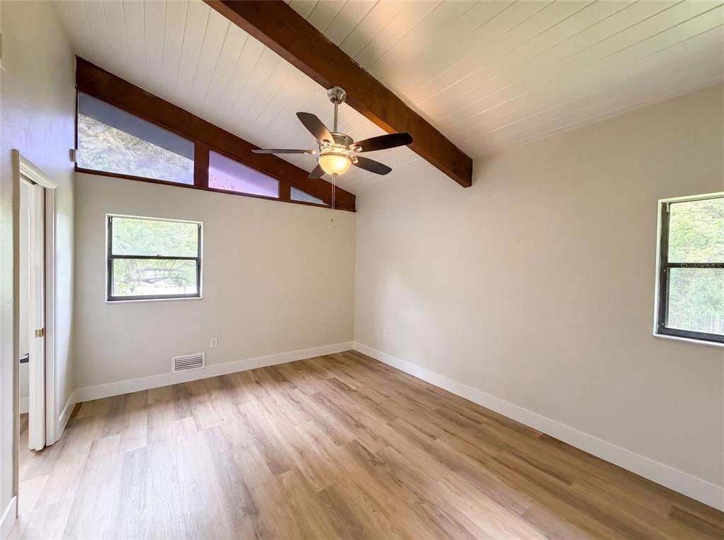 An empty bedroom features wood-look flooring, a vaulted ceiling with exposed beams, and a ceiling fan — 925 PARK PLACE, DELAND, FL