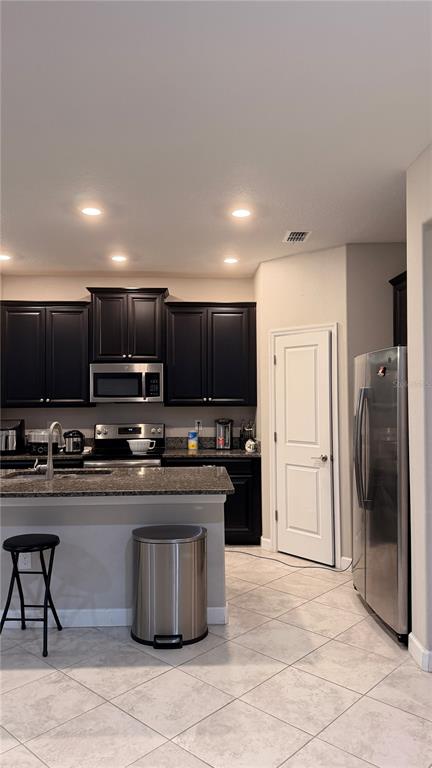 A kitchen features dark cabinetry, granite countertops, a stainless steel refrigerator, and tiled flooring — 9909 VICTORY GALLOP LOOP, RUSKIN, FL