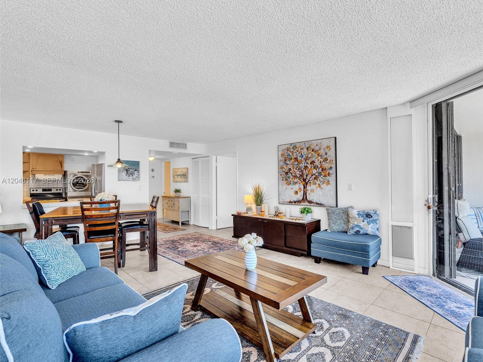 A living and dining area features tile floors, blue furniture, and a large tree painting — 1901 Brickell Ave # B1203, Miami FL 33129, MIAMI, FL