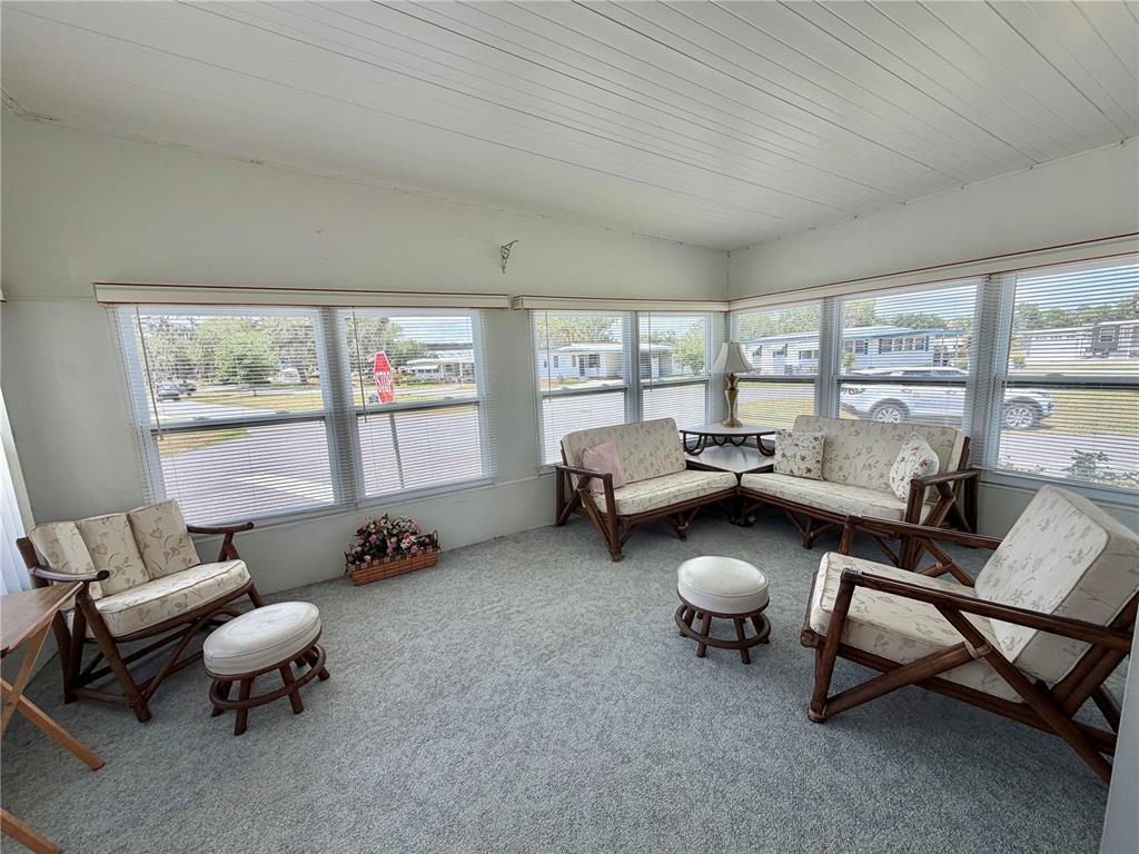 A sunroom features gray carpeting, white paneled walls, multiple windows with blinds, and wicker furniture — 223 HAWTHORNE BOULEVARD, LEESBURG, FL