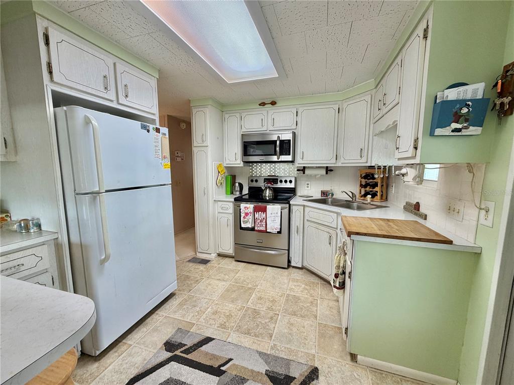 A kitchen features white cabinets, stainless steel appliances, light green walls, and a tiled floor — 223 HAWTHORNE BOULEVARD, LEESBURG, FL