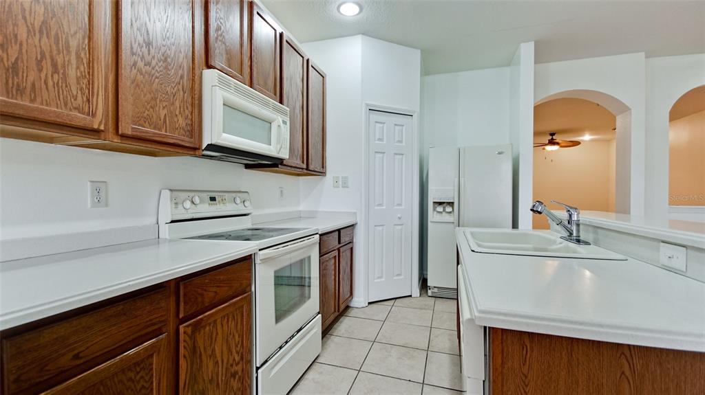 A kitchen features wood cabinets, white appliances, white countertops, and tile flooring — 3497 PARKRIDGE CIRCLE UNIT 16-102, SARASOTA, FL