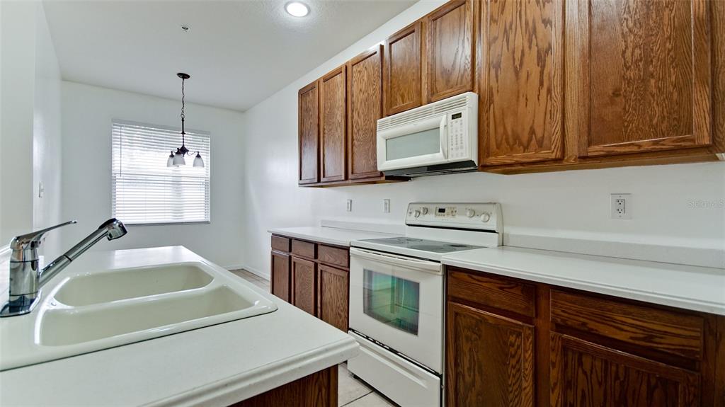 A kitchen features wood cabinets, white countertops, a white stove, and a double-basin sink — 3497 PARKRIDGE CIRCLE UNIT 16-102, SARASOTA, FL