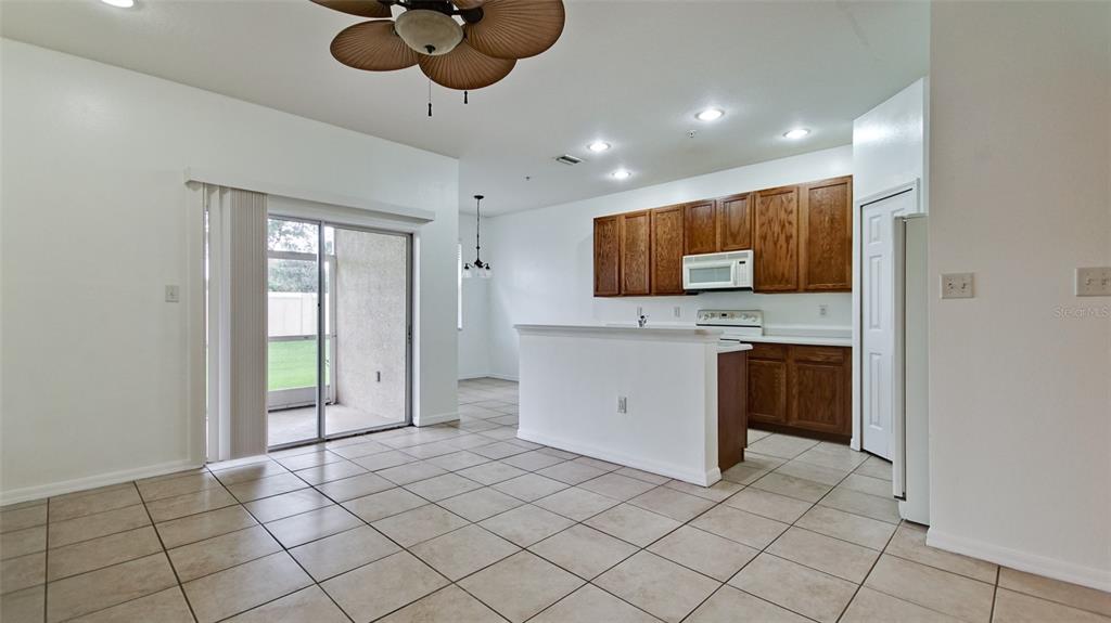 A kitchen and dining area with tile floors, wooden cabinets, and a sliding glass door — 3497 PARKRIDGE CIRCLE UNIT 16-102, SARASOTA, FL