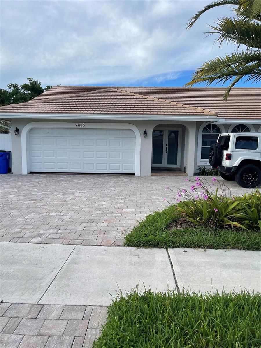 A single-story house exterior features a white garage door, double front doors, and paved driveway — 7485 Royal Palm Boulevard, Margate FL 33063, MARGATE, FL