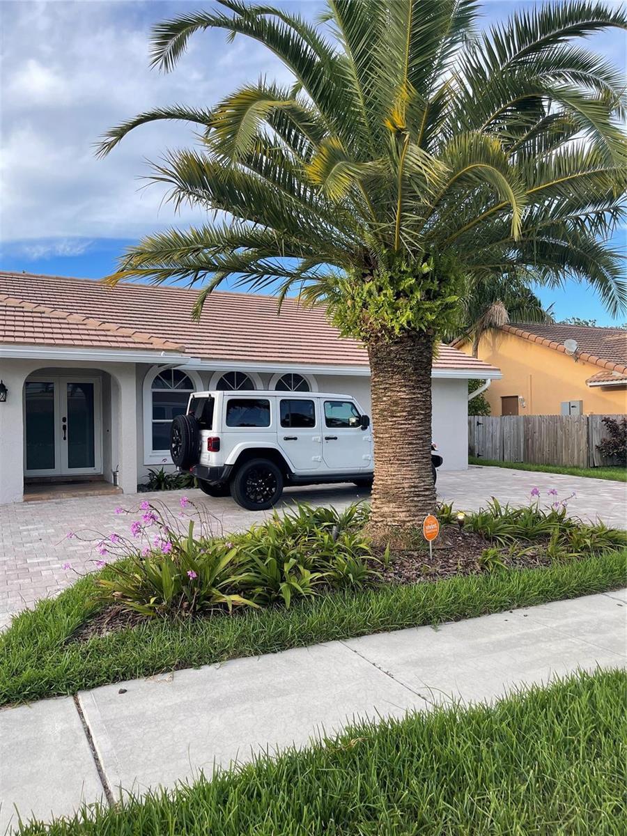 A white Jeep is parked in the driveway of a house with a large palm tree — 7485 Royal Palm Boulevard, Margate FL 33063, MARGATE, FL