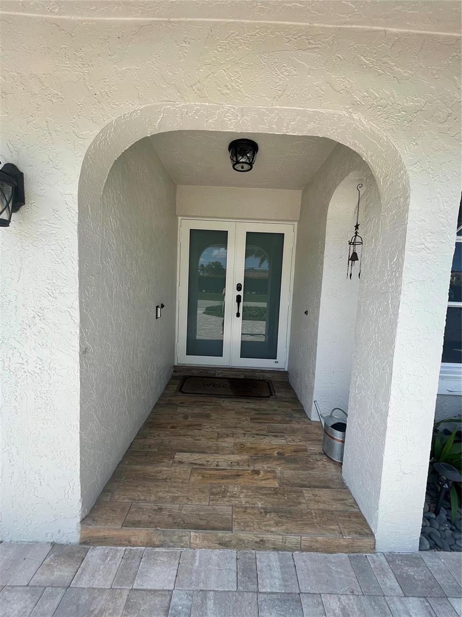 A covered entryway features an arched opening, wood-look tile flooring, and double glass doors — 7485 Royal Palm Boulevard, Margate FL 33063, MARGATE, FL