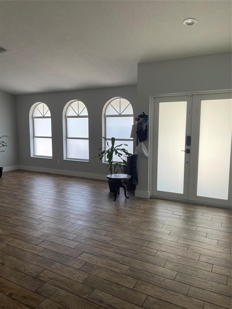 A bright room features wood-look tile flooring, three arched windows, and double glass entry doors — 7485 Royal Palm Boulevard, Margate FL 33063, MARGATE, FL