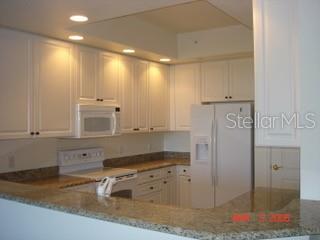 A kitchen features white cabinets, granite countertops, a white refrigerator, and a ceiling fan — 261 MINORCA BEACH WAY UNIT 203, NEW SMYRNA BEACH, FL