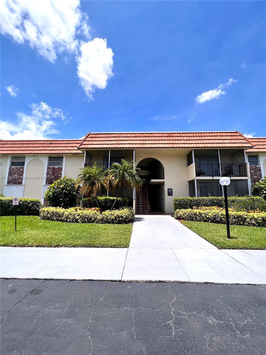 A two-story apartment building features a tan stucco exterior, a tiled roof, and palm trees — 22755 SW 66th Avenue # 103, Boca Raton FL 33428, BOCA RATON, FL