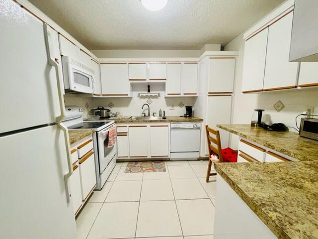 A kitchen features white cabinets, speckled countertops, white appliances, and light-colored tile flooring — 22755 SW 66th Avenue # 103, Boca Raton FL 33428, BOCA RATON, FL