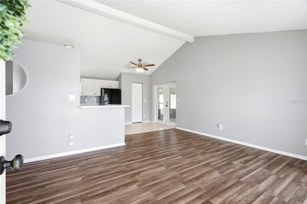 A living room with wood-look flooring opens to a kitchen featuring white cabinets and appliances — 8704 MARLIN COURT, TAMPA, FL