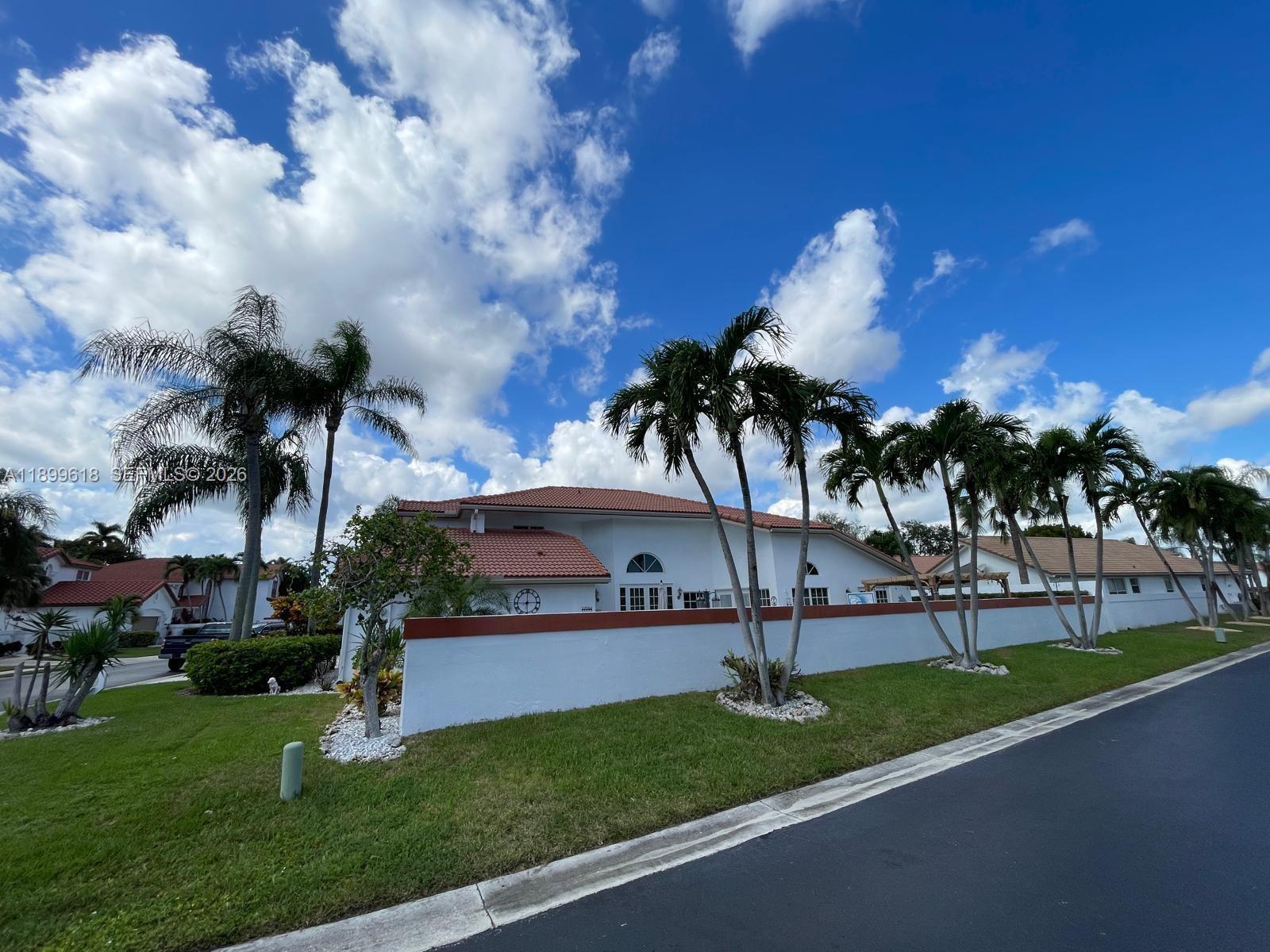 A white house with a red tile roof sits behind a low wall with palm trees — 6953 Columbia Court, Margate FL 33063, MARGATE, FL
