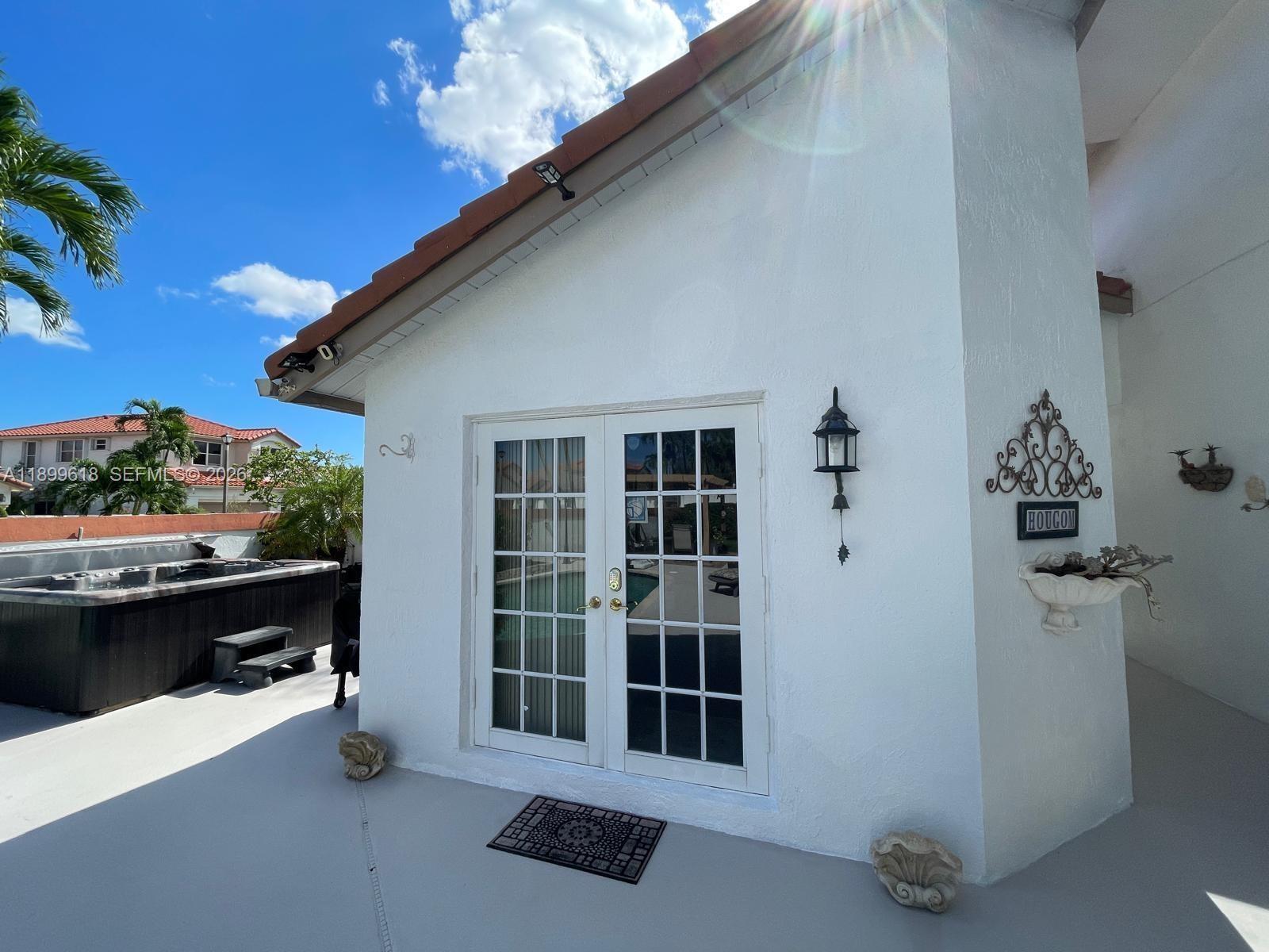 A white exterior wall features French doors, a wall-mounted lantern, and a nearby hot tub — 6953 Columbia Court, Margate FL 33063, MARGATE, FL