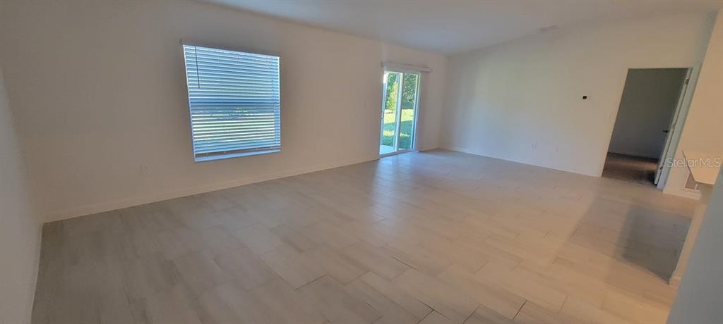 An empty living room features light-colored tile flooring, white walls, a window, and sliding glass doors — 10083 GENTLE RAIN DRIVE, LAND O LAKES, FL