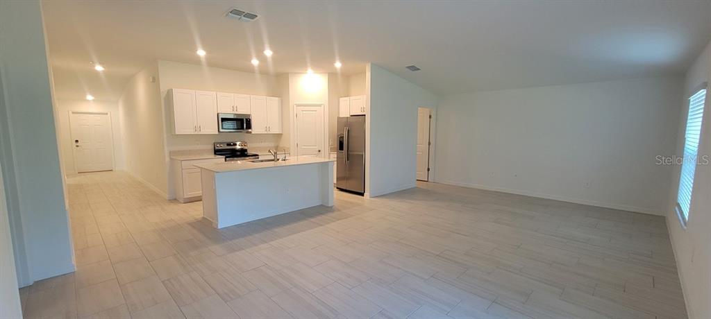 An open-concept kitchen with white cabinets and a center island overlooks a spacious living area — 10083 GENTLE RAIN DRIVE, LAND O LAKES, FL