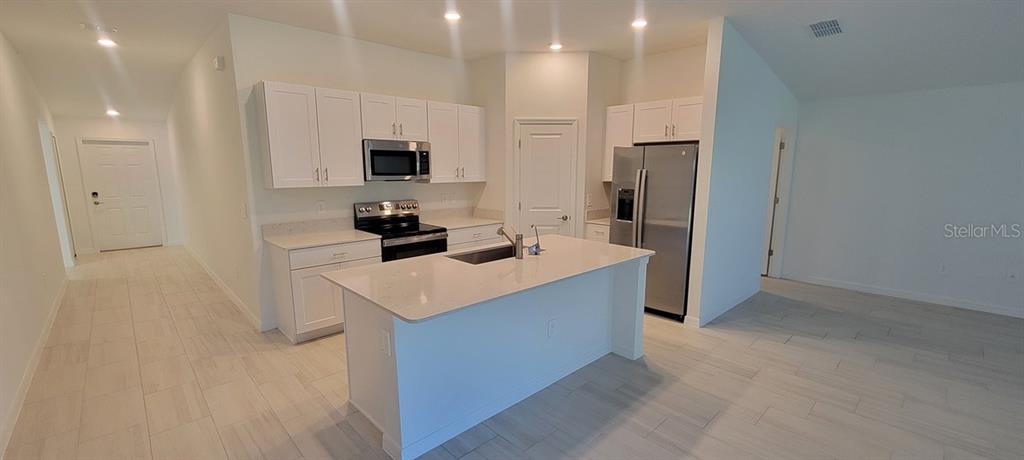 A kitchen features white cabinetry, stainless steel appliances, a center island, and light-colored tile flooring — 10083 GENTLE RAIN DRIVE, LAND O LAKES, FL