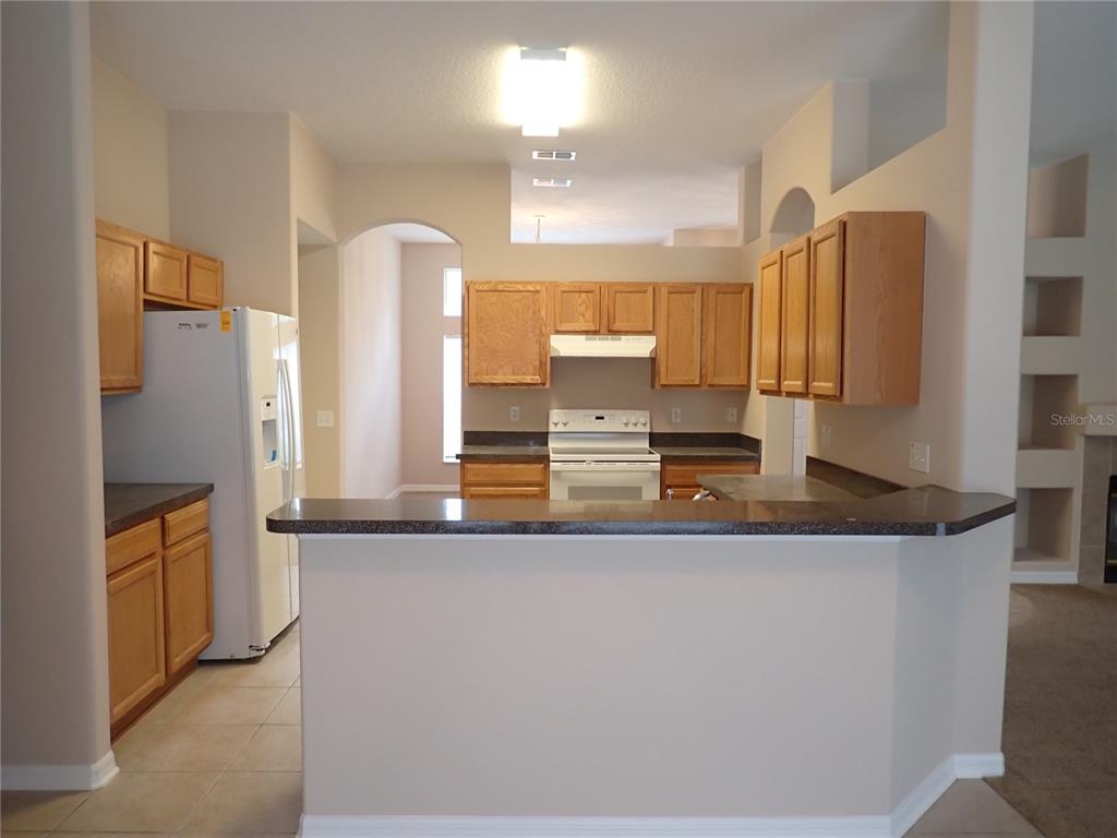 A kitchen features light wood cabinets, white appliances, and a dark countertop breakfast bar — 132 BERKSHIRE LANE, PALM COAST, FL
