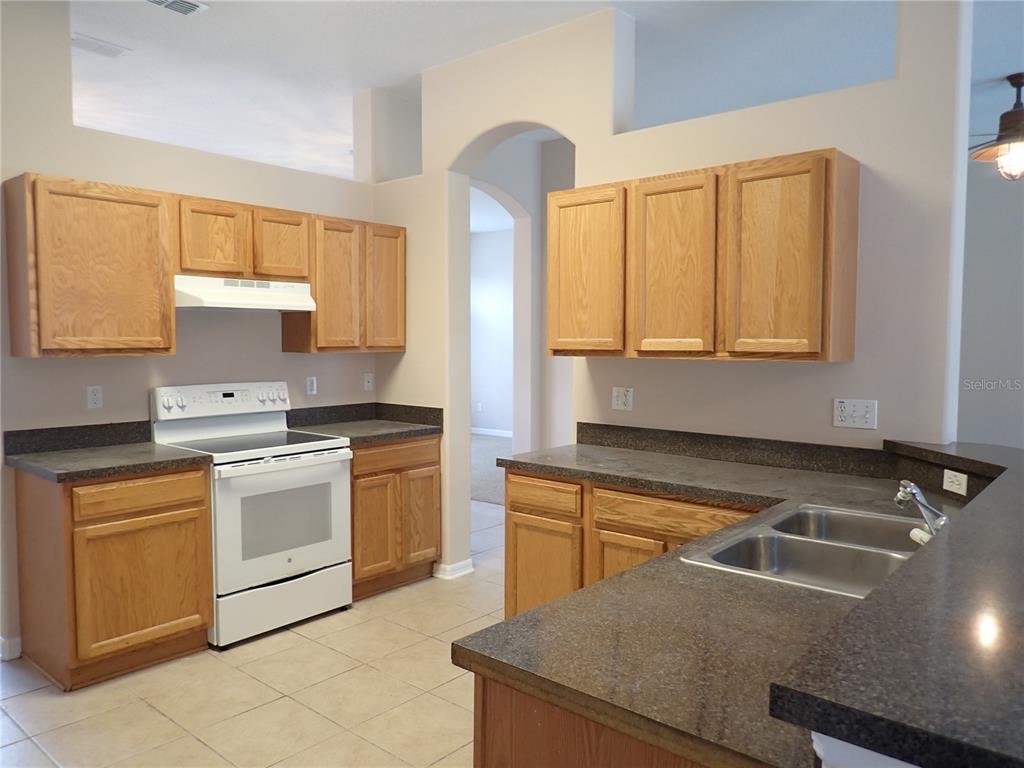 A kitchen features oak cabinets, dark countertops, a white stove, and light-colored tile flooring — 132 BERKSHIRE LANE, PALM COAST, FL