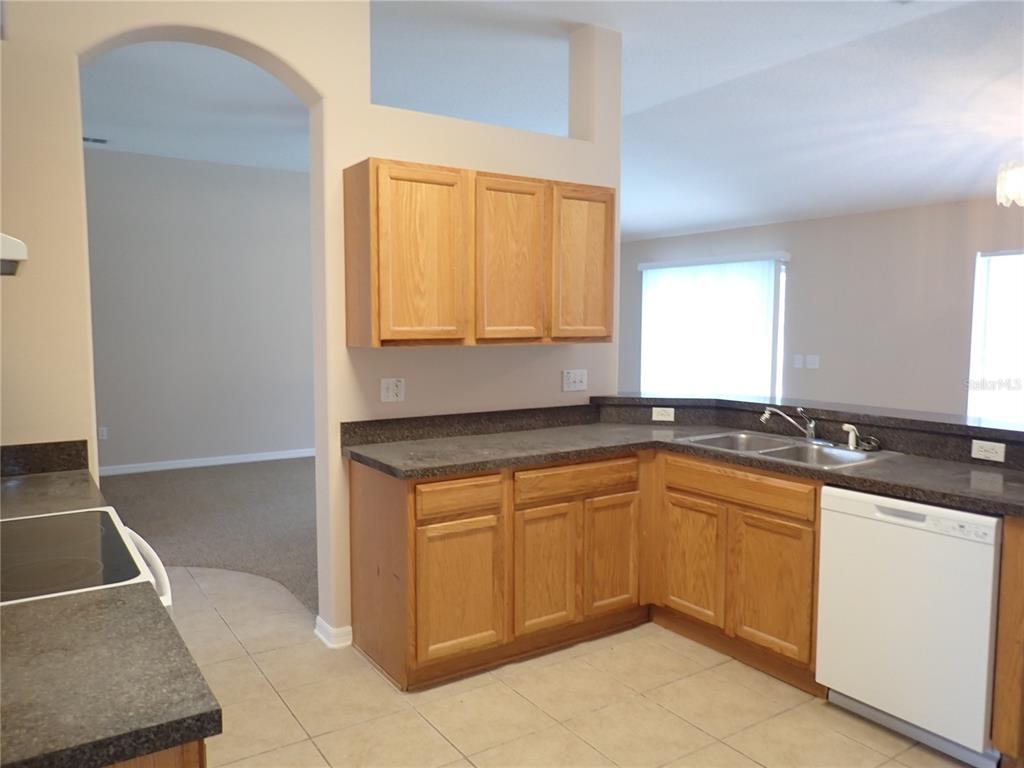 A kitchen features light wood cabinets, dark laminate countertops, and a white dishwasher — 132 BERKSHIRE LANE, PALM COAST, FL