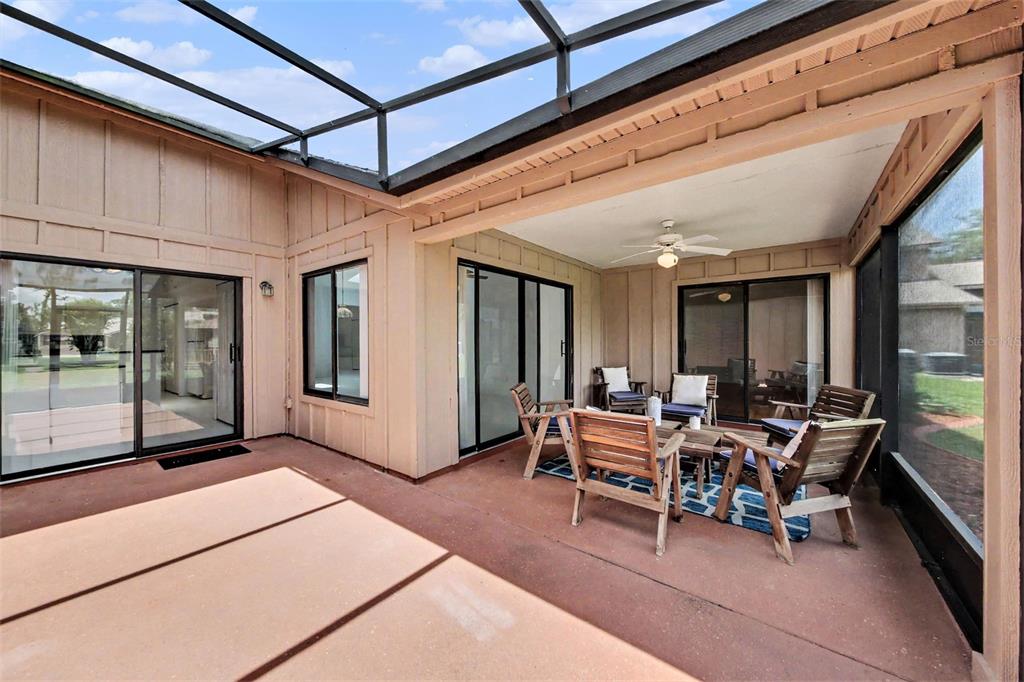 A screened-in patio features a concrete floor, wooden furniture, and sliding glass doors — 1914 SPRUCEWOOD WAY, PORT ORANGE, FL