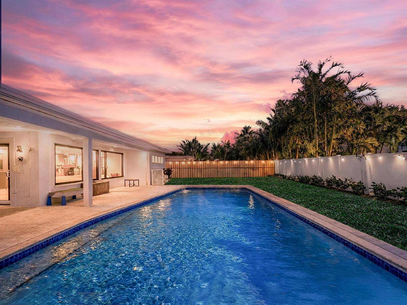 A backyard swimming pool sits next to a house patio under a pink sunset sky — 1098 W Camino Real, Boca Raton FL 33486, BOCA RATON, FL