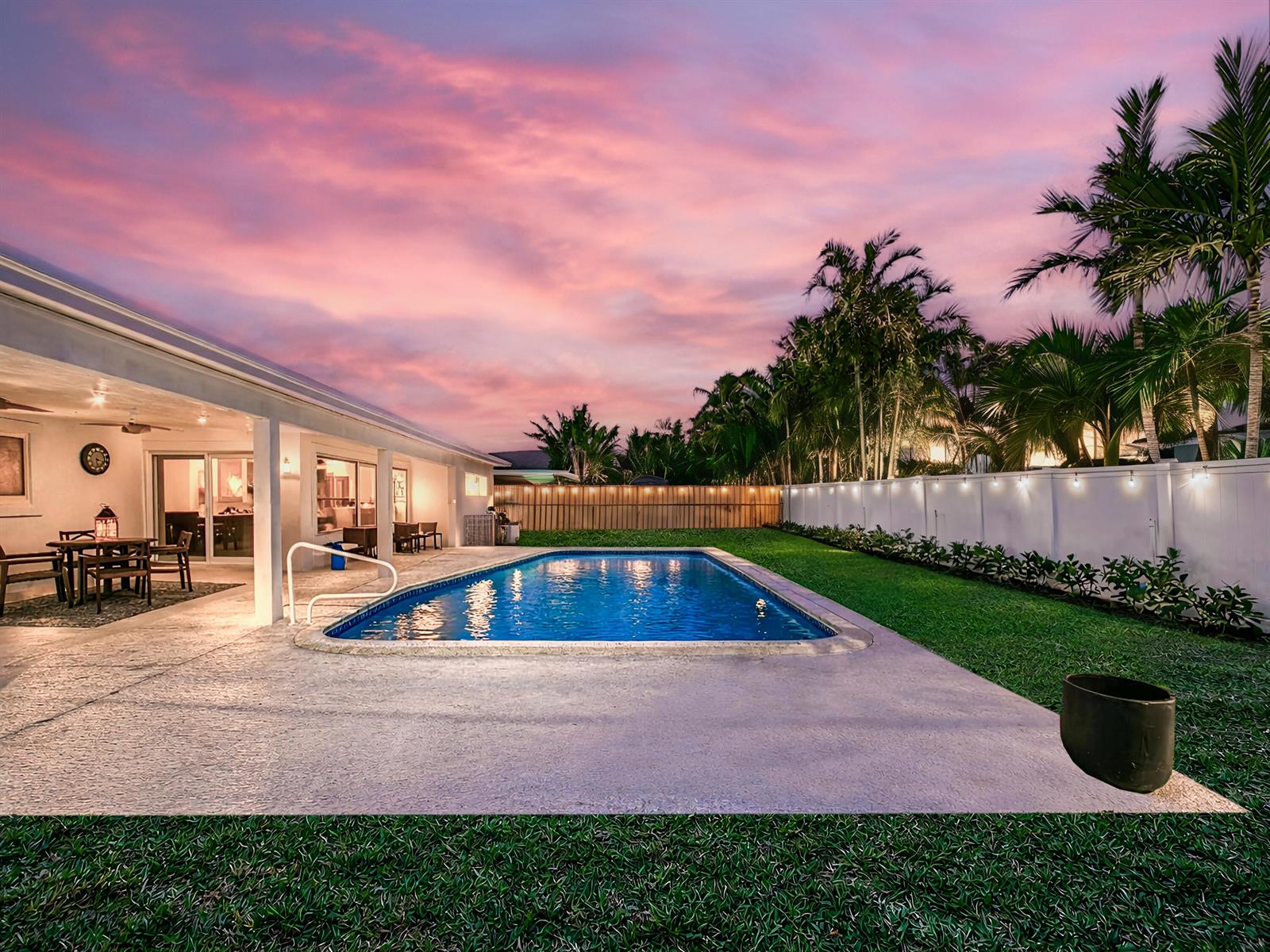 A backyard features a rectangular swimming pool, a concrete patio, and a lawn at sunset — 1098 W Camino Real, Boca Raton FL 33486, BOCA RATON, FL