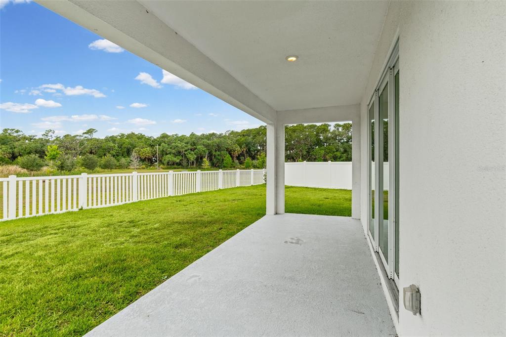 A covered concrete patio overlooks a grassy backyard enclosed by a white vinyl fence — 8093 TEA OLIVE TERRACE, PALMETTO, FL