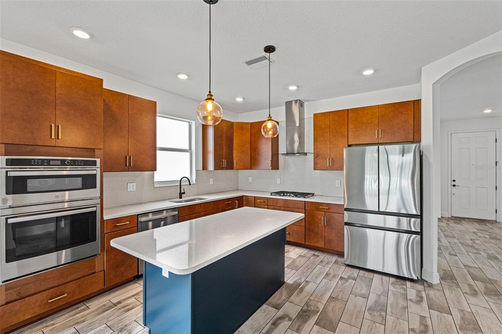 A kitchen features wood cabinets, a blue island, stainless steel appliances, and light-colored countertops — 8093 TEA OLIVE TERRACE, PALMETTO, FL