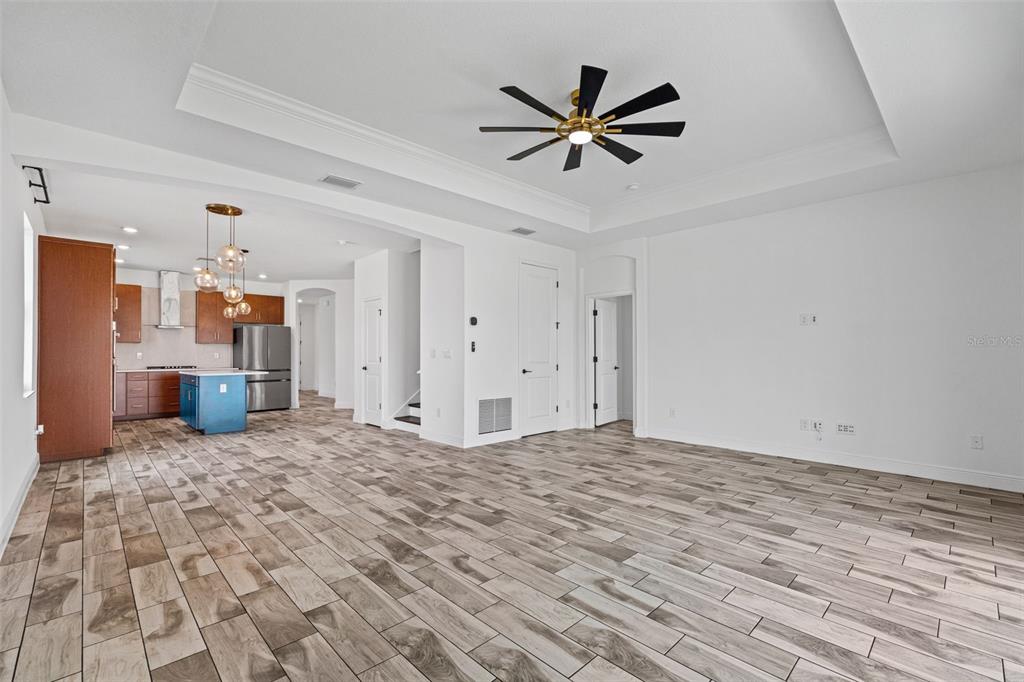 An open-concept living area features wood-look tile flooring, a tray ceiling, and a modern kitchen — 8093 TEA OLIVE TERRACE, PALMETTO, FL