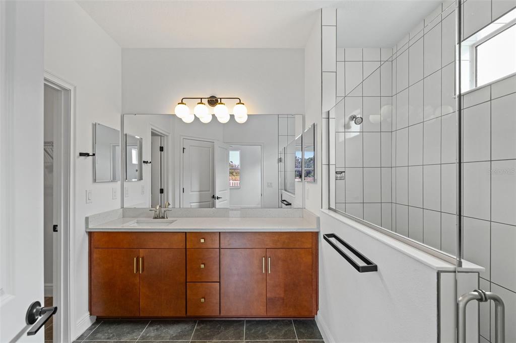 A bathroom features a wood vanity with a white countertop, a mirror, and a shower — 8093 TEA OLIVE TERRACE, PALMETTO, FL