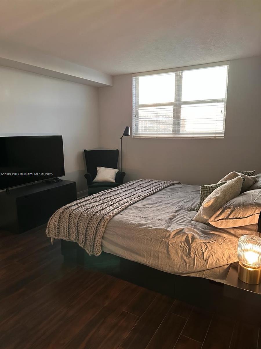 A bedroom features a bed with a chunky knit throw, a television, and dark flooring — 3000 S Ocean Dr # 612, Hollywood FL 33019, HOLLYWOOD, FL