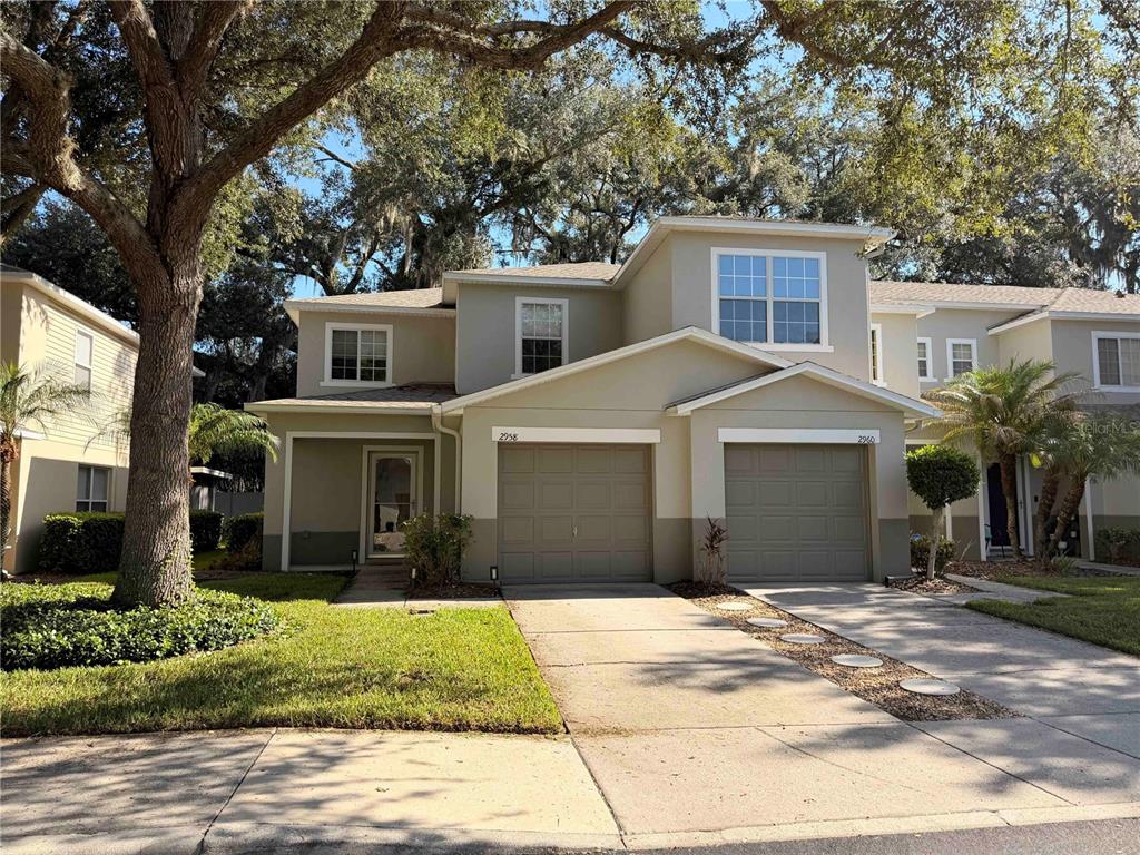 A two-story duplex with tan stucco siding, two garage doors, and a large oak tree — 2958 ROYAL TUSCAN LANE, VALRICO, FL