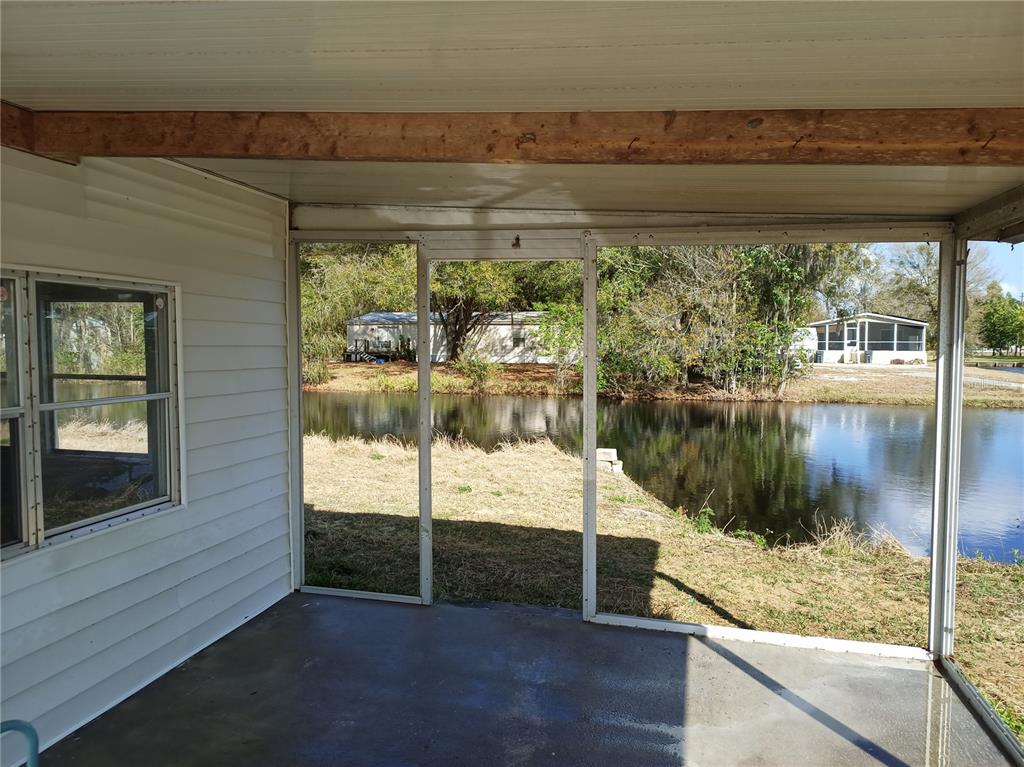 A screened-in porch with a concrete floor overlooks a small pond and neighboring homes — 3368 MAPLE LANE, HAINES CITY, FL