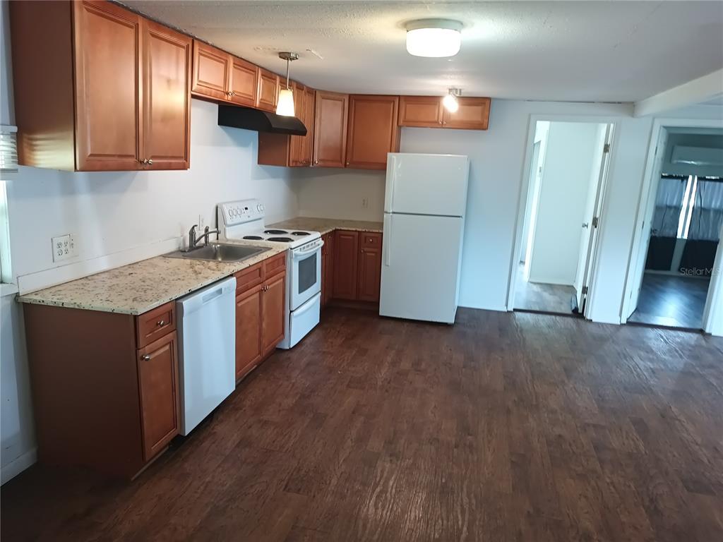 A kitchen features wood cabinets, granite countertops, white appliances, and wood-look flooring — 3368 MAPLE LANE, HAINES CITY, FL
