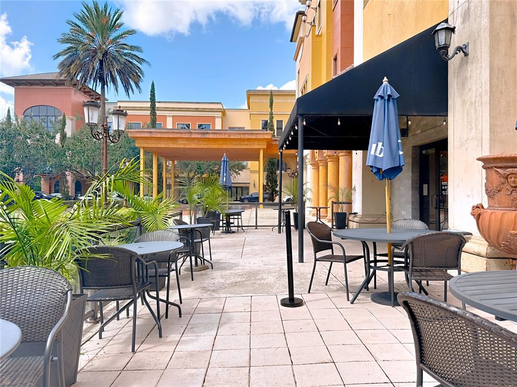 An outdoor patio features several tables with chairs and umbrellas under a black awning — 6996 PIAZZA GRANDE AVENUE UNIT 100, ORLANDO, FL