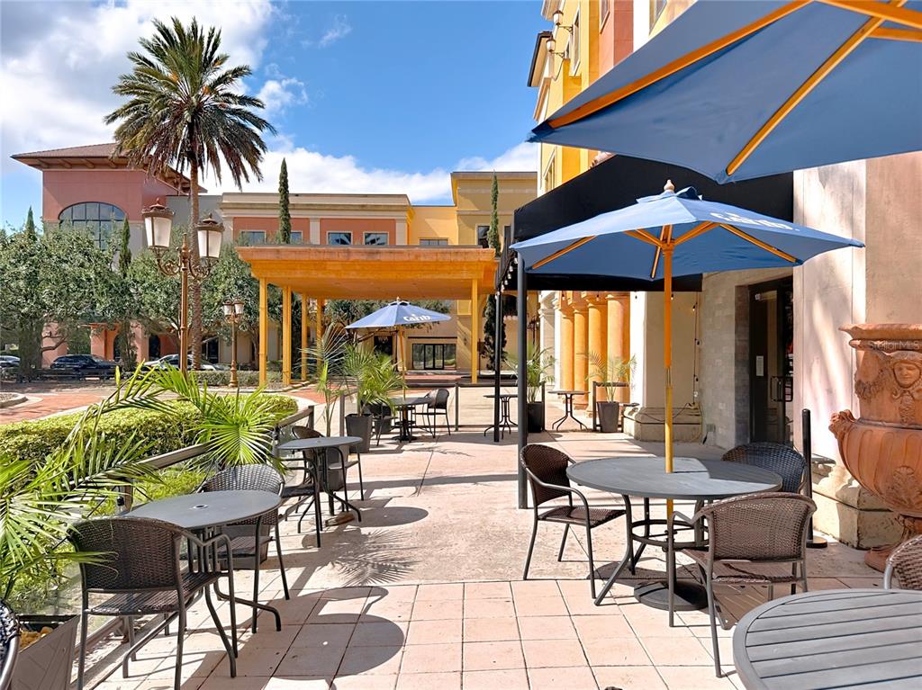 An outdoor patio features several tables with blue umbrellas and chairs near a building entrance — 6996 PIAZZA GRANDE AVENUE UNIT 100, ORLANDO, FL