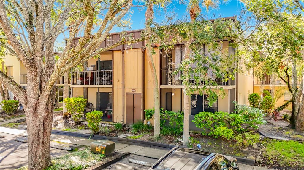 A two-story apartment building with balconies and tan siding is surrounded by trees and landscaping — 11805 RAINTREE LAKE LN UNIT B, TEMPLE TERRACE, FL