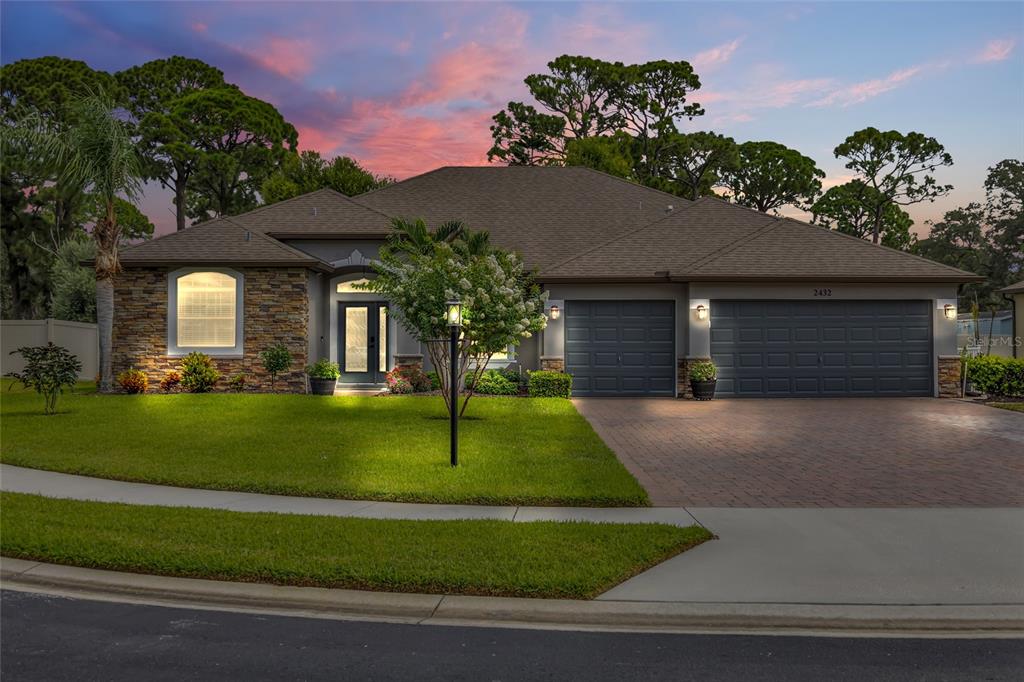 A single-story house with a stone facade, gray exterior, and a paved driveway at dusk — 2432 OKALANI STREET, MELBOURNE, FL