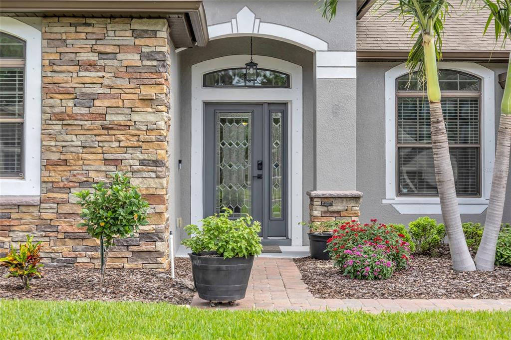 The front entrance of a house features a stone facade, gray door, and landscaping — 2432 OKALANI STREET, MELBOURNE, FL