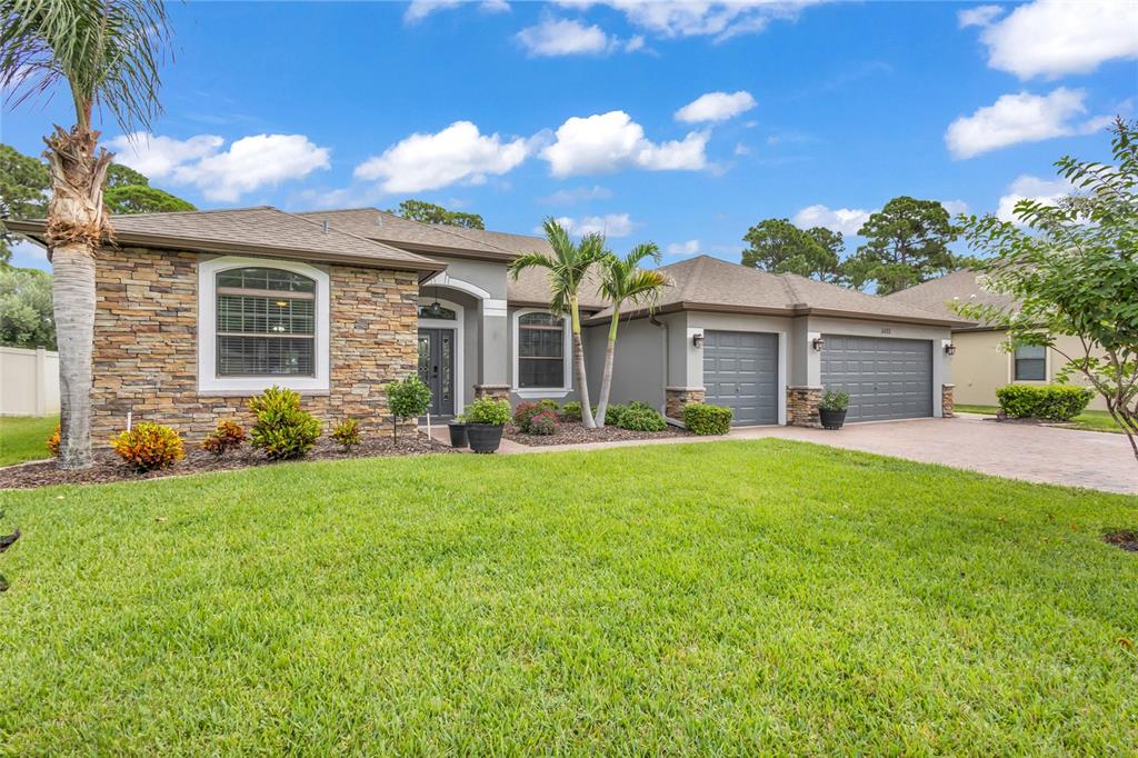 A single-story house with a stone facade, gray garage doors, and a manicured front lawn — 2432 OKALANI STREET, MELBOURNE, FL