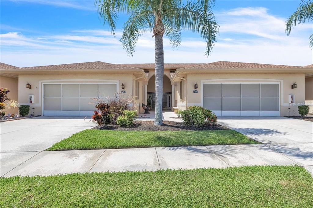 A single-story duplex with two garage doors, a central entryway, and a palm tree — 24057 PARK PLACE DRIVE S UNIT 51, PUNTA GORDA, FL
