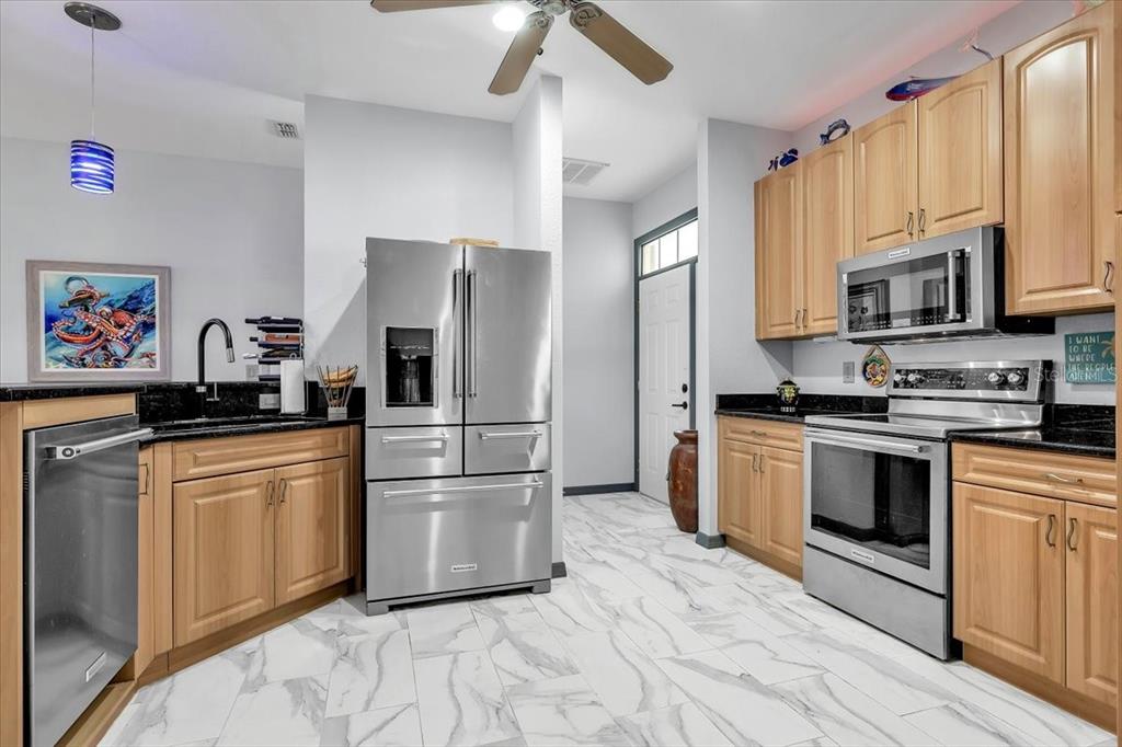 A kitchen with light wood cabinets, stainless steel appliances, and white marble-patterned tile flooring — 24057 PARK PLACE DRIVE S UNIT 51, PUNTA GORDA, FL